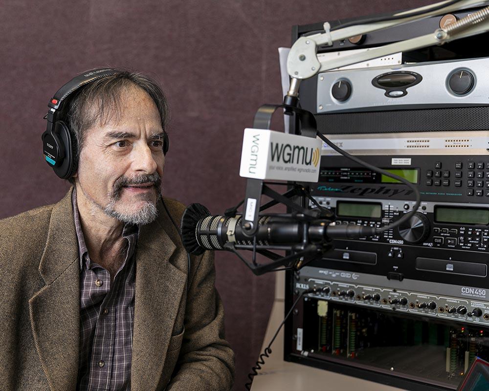 Dr. Peter Becker wears headphones and speaks into the microphone during Access to Excellence podcast recording